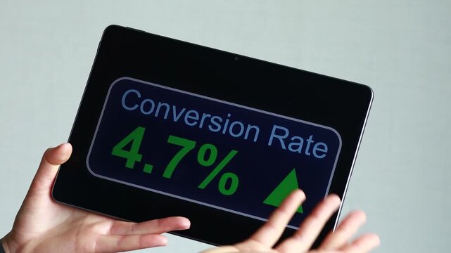 A person is holding a tablet that displays a conversion rate of 4.7 percent. The rate shows an upward trend. This scene takes place indoors.
