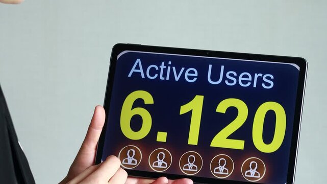 A person is holding a tablet that shows the count of active users as 6,120. The setting appears to be a business environment with a light background.