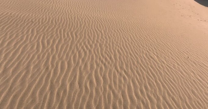 Aerial view tracking over rippled desert sand dunes with wind patterns and smooth golden texture in warm light
