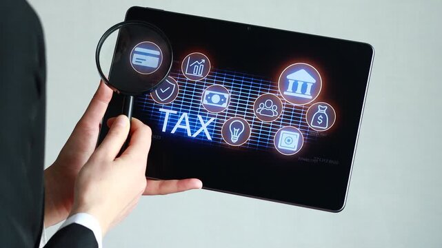 A person holds a tablet while examining tax-related data. The screen shows various icons including charts, money, and buildings. This scene takes place in an office setting.