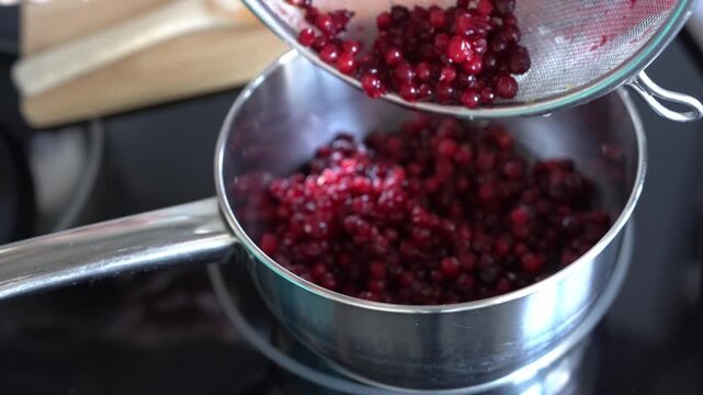 A woman makes lingonberry jam in her home kitchen. Jam is made on an induction stove.