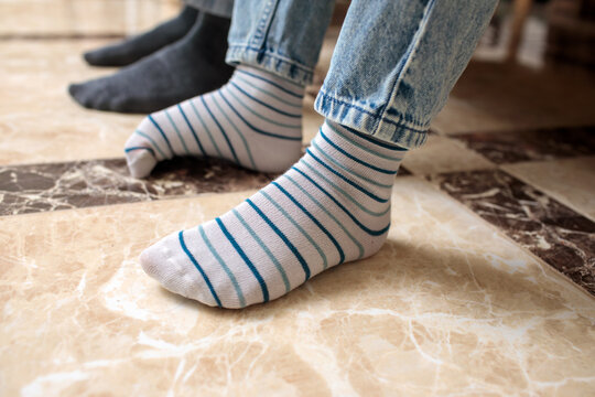 Two pairs of feet in different socks on marble floor, white striped socks and dark grey ankle socks with jeans