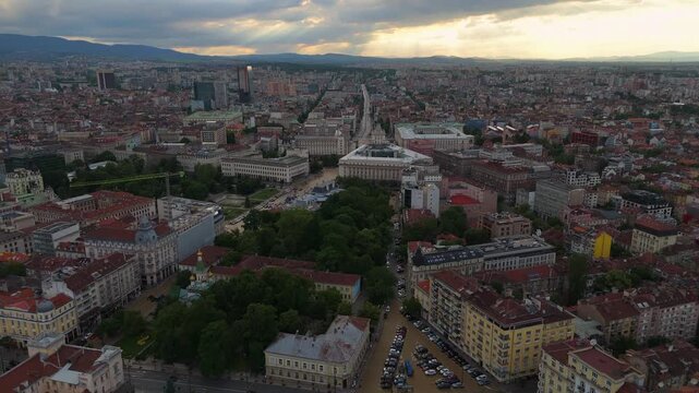 High angle drone panorama overlooking the government buildings and busy avenues of Sofia city center during a dramatic twilight sunset in Bulgaria