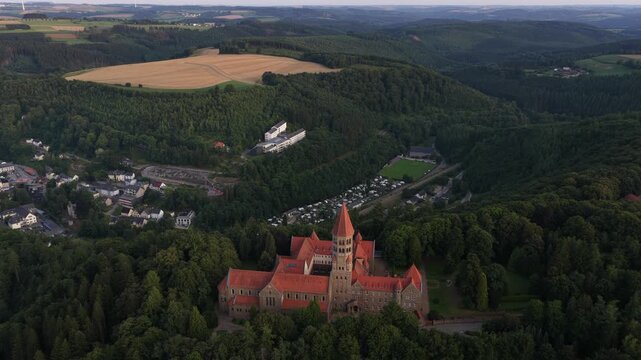 Expansive aerial perspective capturing the historic maria laach abbey, a benedictine monastery, beautifully situated amidst the dense green forests and rolling hills of the eifel region in germany