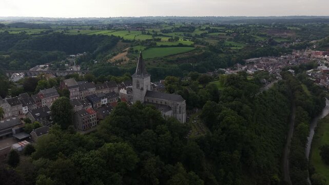 High angle drone shot capturing the historic city of thuin in belgium, featuring its famous belfry and the sambre river surrounded by a lush green valley and traditional houses