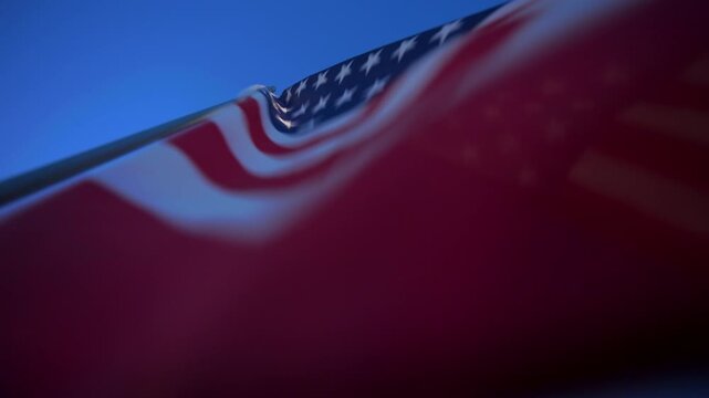 American flag billows majestically against a clear deep blue sky on a sunny day. Red and white stripes ripple while white stars on blue canton catch sunlight. Shallow depth of field creates soft.