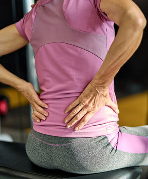 Senior mature woman exercising at gym, suffering a back pain, neck pain,  injury health care