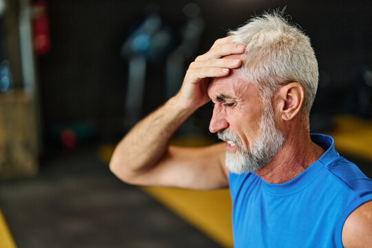 Senior mature man exercising at gym, suffering a headache migraine pain or injury health care