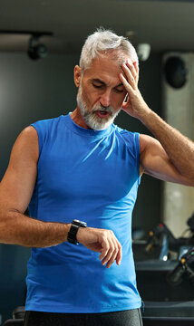 Portrait of a senior man exercising in a gym, mature male running using treadmill machine and checking smart watch for performance, healthy lifestyle and cardio exercise at fitness club concepts, vita