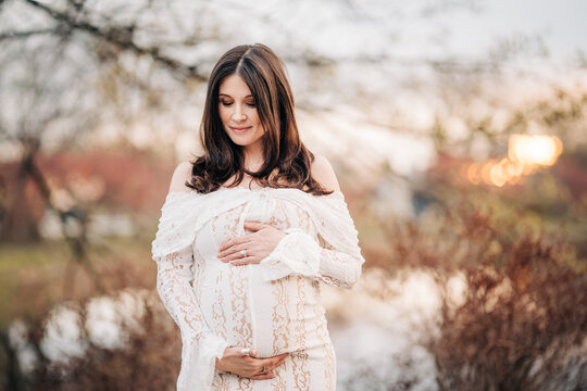 Pregnant woman embracing belly during outdoor sunset maternity session