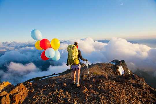 Woman with balloons hikes on a mountain summit