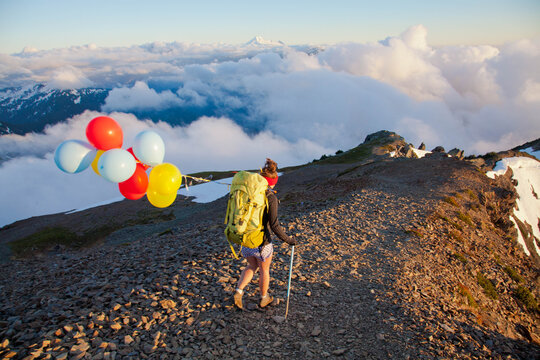 Woman with backpack and balloons hiking above clouds