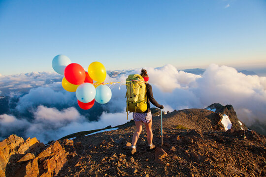 Hiker with colorful balloons reaches a mountain summit