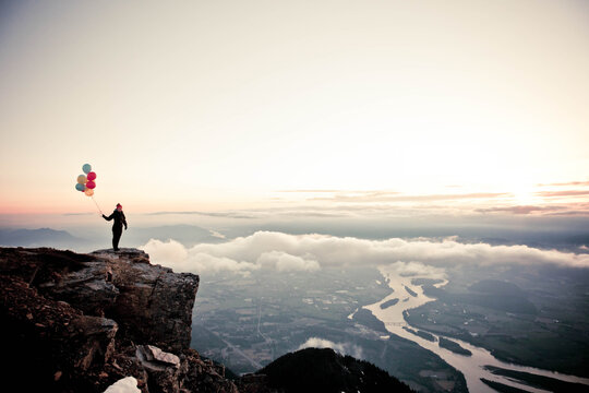 Woman holds balloons on mountain with scenic view