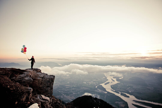silhouette woman holds balloons on mountain summit.