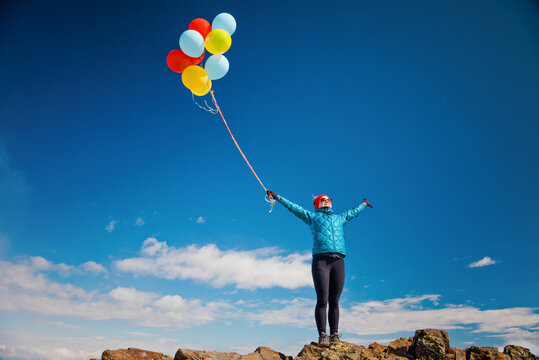 Fit woman celebrates with balloons on mountain summit.