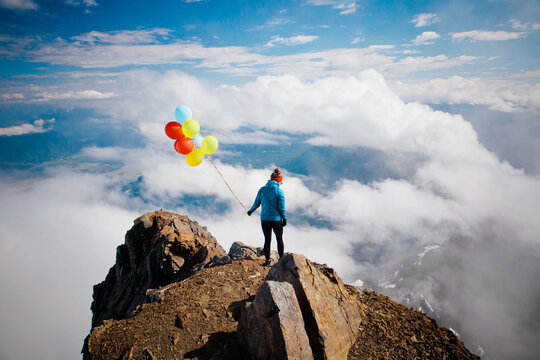 Woman with balloons on a mountain peak above the clouds