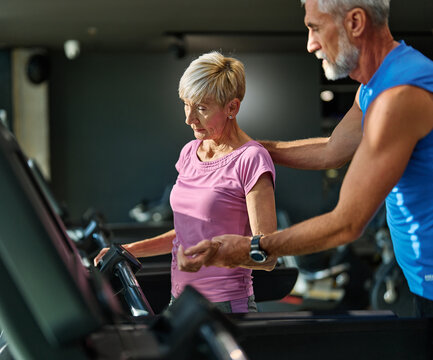 Portrait of a senior couple exercising in a gym, mature couple running using treadmill , healthy lifestyle and cardio vitality and active senior, coach training help and support, checking heartbeat