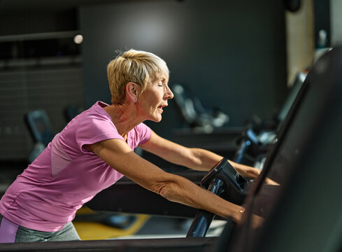 Portrait of a senior elderly woman exercising in a gym, tired mature female running and taking a break using treadmill, healthy lifestyle and cardio exercise at fitness club concepts, vitality and act