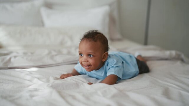 African american infant lying on stomach in bed, cute little child explore life. Charming black infant girl or boy enjoying beautiful day, happy family, motherhood and childhood, healthy african baby