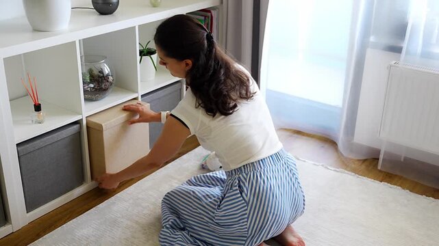 Young woman using storage box from shelving system in home interior. Home organization and decluttering routine concept