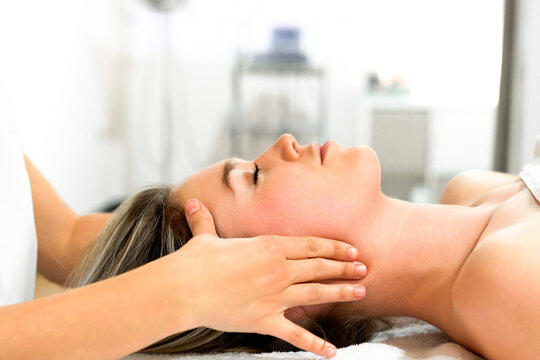 Relaxed woman receiving gentle neck and jaw massage in bright treatment room