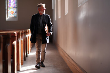 Obraz premium Elderly man walking with folder along church aisle interior