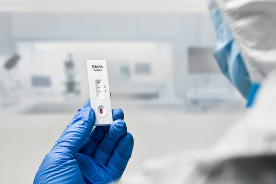 A gloved scientist holds a positive Ebola antigen rapid test cassette inside a sterile laboratory setting