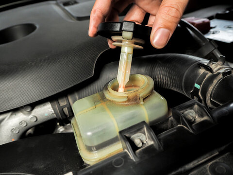 A mechanic opens the power steering fluid reservoir cap with an attached dipstick under the hood of a car engine bay