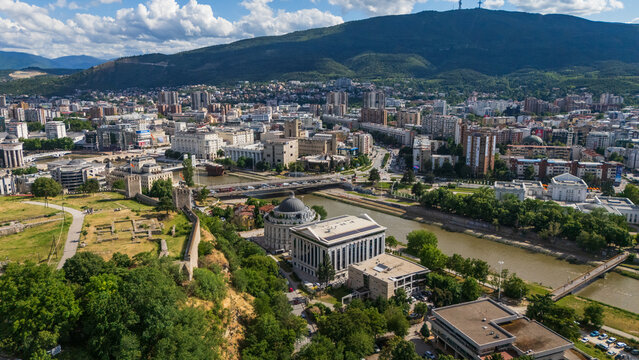 High angle drone view of Skopje city center with the Vardar river, stone bridges, and historic Kale Fortress walls against Vodno mountain, North Macedonia