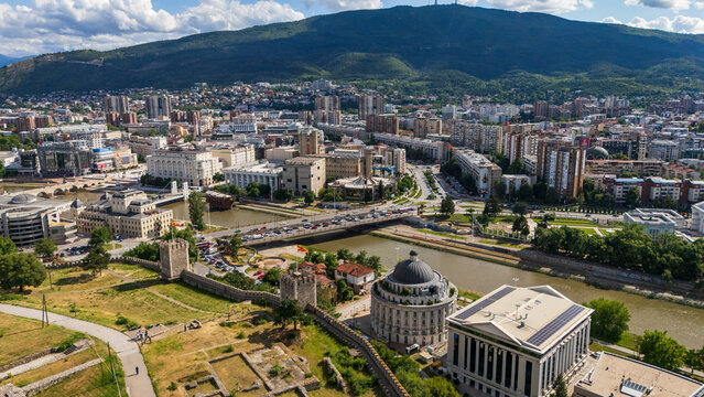 High angle drone view of Skopje city center with the Vardar river, stone bridges, and historic Kale Fortress walls against Vodno mountain, North Macedonia