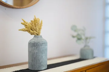 Fototapete Japandi A modern interior setup featuring yellow dried flowers in a textured grey ceramic vase on a wooden console table with a shallow depth of field.  © Rijjal