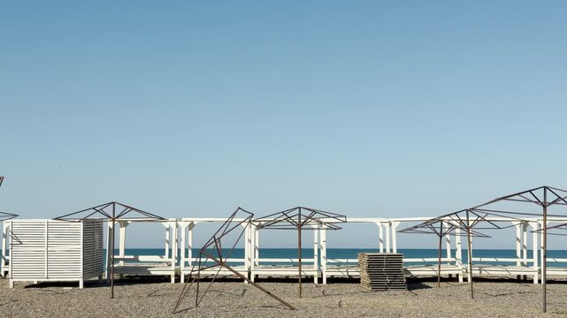 Row of white cabanas and metal sunshade frames stand deserted on the gravel shore. The quiet sea and sky create a peaceful feeling of solitude. It feels like a calm and lonely seaside escape.