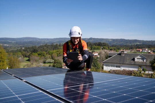 Technician inspecting solar panel on a rooftop with a tablet