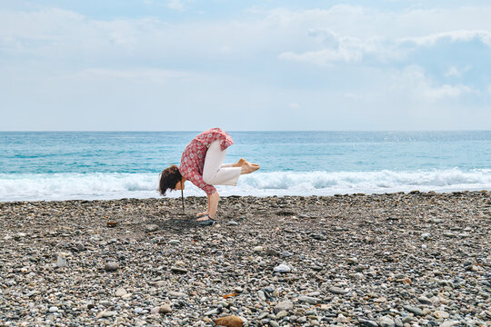 Woman practicing yoga outdoors on pebble beach for wellness