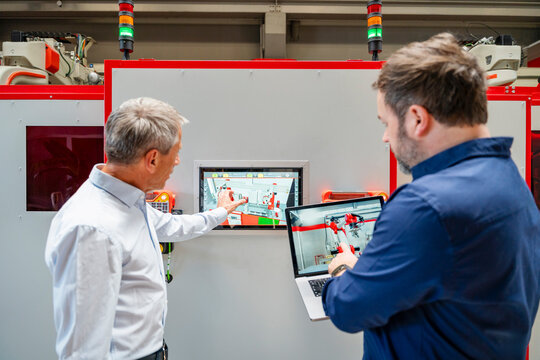 Colleagues discussing robot automation on laptop in factory