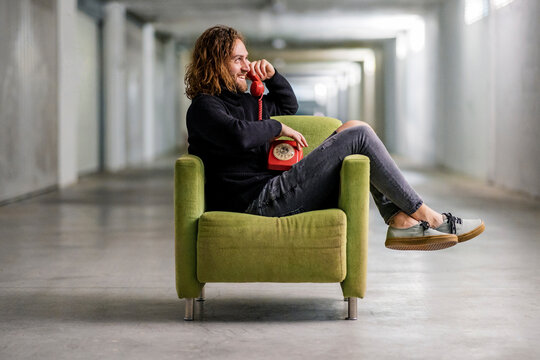 Smiling man talking over telephone while sitting on armchair at home