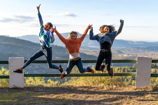 Excited friends holding hands jumping together on sunny day
