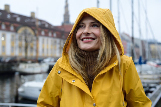 Denmark, Copenhagen, portrait of happy woman at city harbour in rainy weather