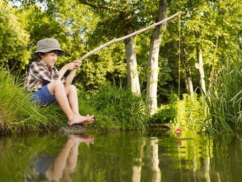 Child fishing with a stick by a stream in summer