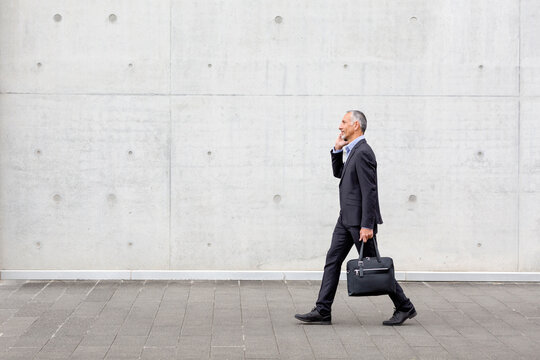 Male professional with briefcase walking while talking on smart phone