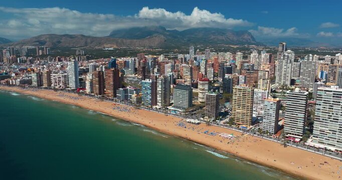 Benidorm aerial coastline right side skyscrapers sandy beach Mediterranean Spain Alicante summer drone panorama turquoise sea mountain clouds travel resort slow motion tourism destination