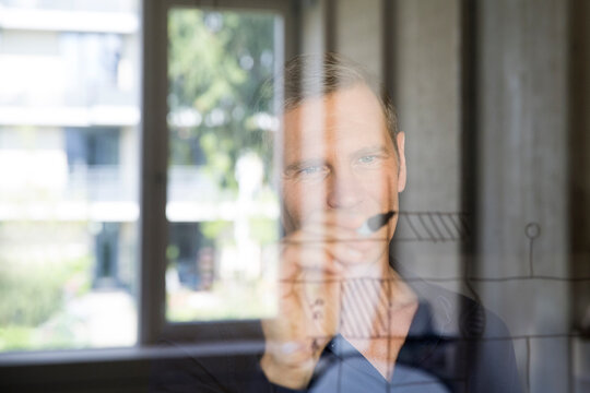 Portrait of business man drawing sketch on glass pane
