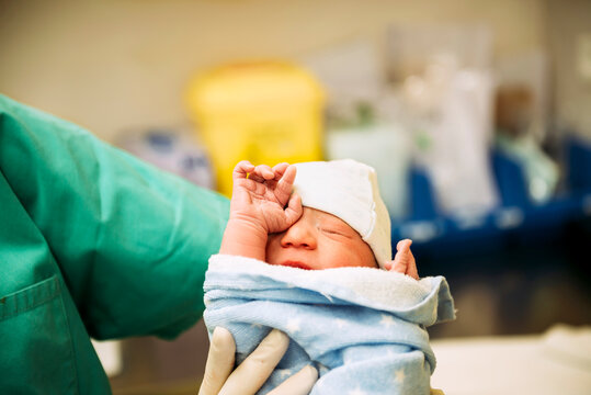 Newborn girl wrapped in a towel holded by the doctor in the delivery room