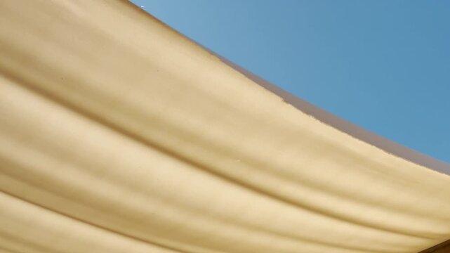 A soft cream fabric awning extends across the view against a clear blue sky. This simple, bright scene brings a feeling of warm comfort, relaxation, and peaceful summer vibes.