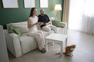 Obraz premium Cute man and woman playing game by joysticks on sofa at home