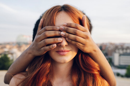 Woman covering eyes of redhead girlfriend with hands at sunset