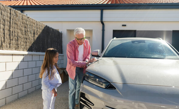Happy grandfather and granddaughter cleaning a car in the backyard