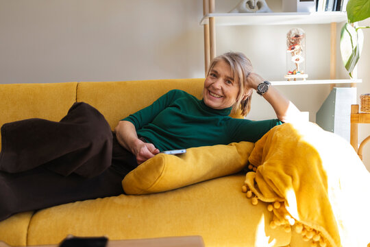 Smiling woman relaxing on a yellow sofa at home with a smartphone