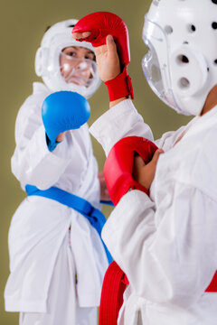 Karate fighter presses a red gloved punch directly into the opponent's blue helmeted face at close quarters, capturing raw contact and defensive struggle in an intense grappling and striking exchange.